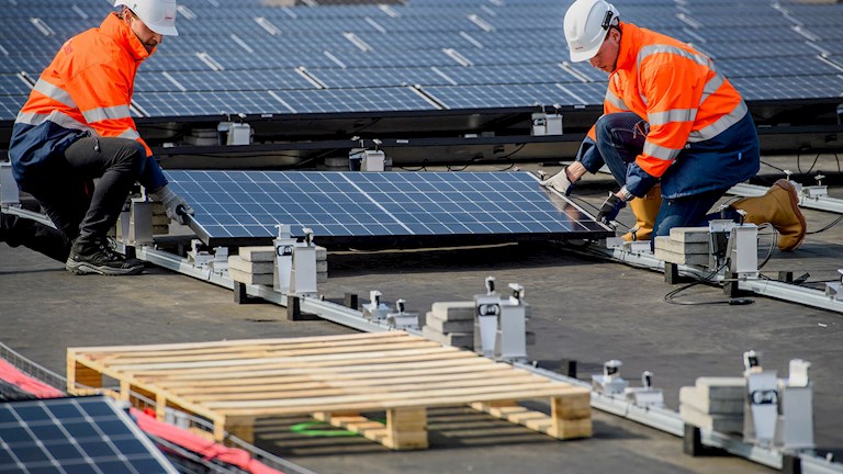 Twee Eneco medewerkers plaatsen een zonnepaneel op het dak van Kingspan