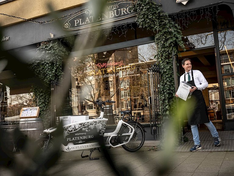 Julien Platenburg bij zijn winkel met de elektrische bakfiets op de voorgrond