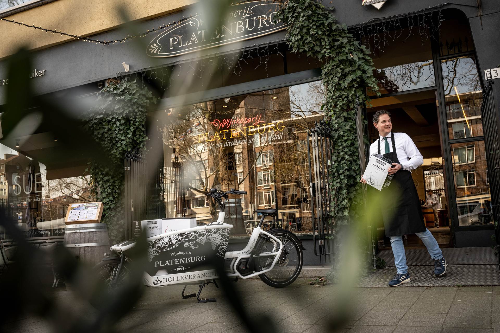 Julien Platenburg bij zijn winkel met de elektrische bakfiets op de voorgrond