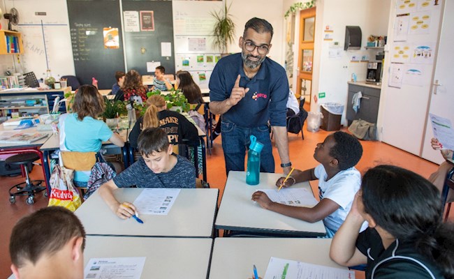 Ewald Gobind, custom engineer bij Eneco, staat in een klaslokaal op de basisschool en geeft een gastles over duurzame energie