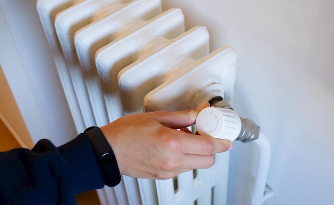 Een hand draait aan de knop van een radiator.