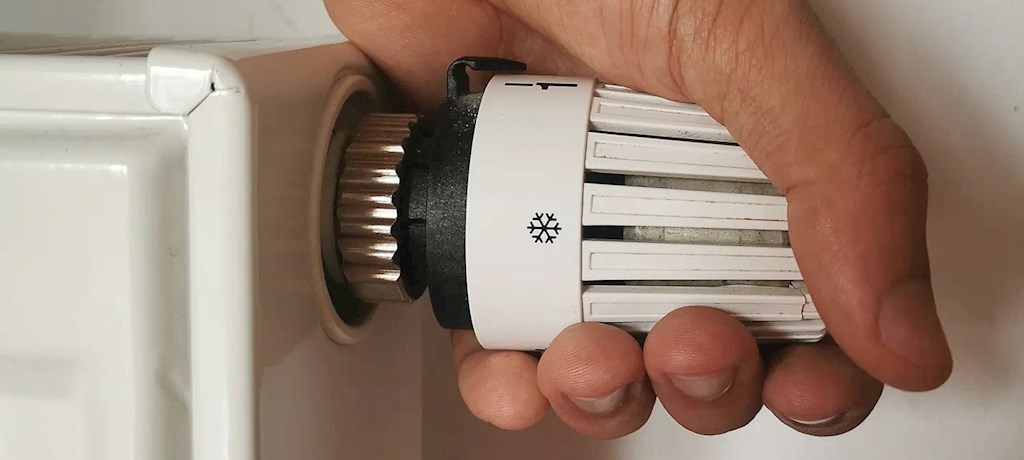 Een hand draait aan de radiatorknop