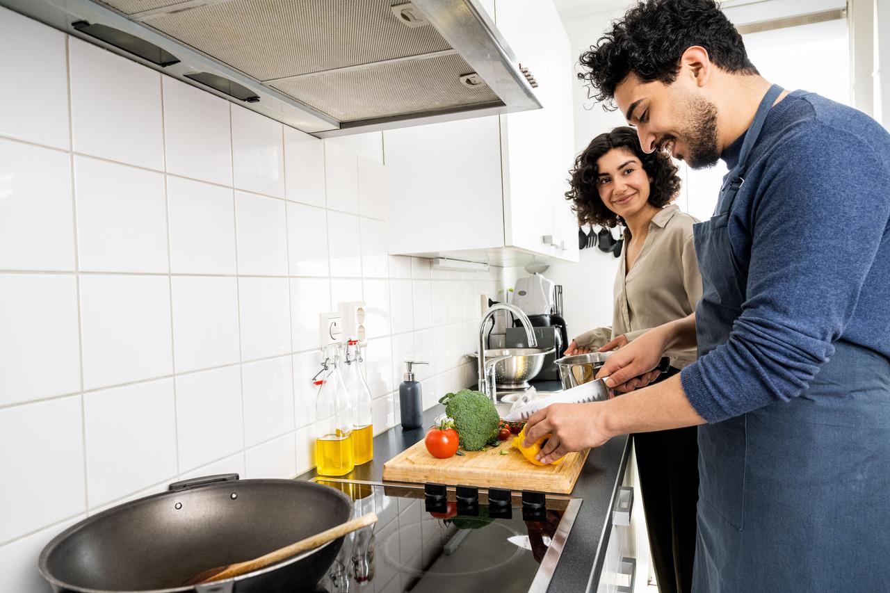 Een man en vrouw zijn samen in de keuken aan het koken op inductie.