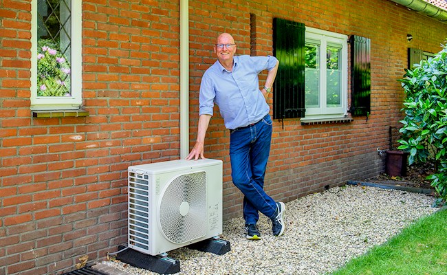 Warmtepomp eigenaar Jan Hoorn staat glimlachend naast de buitenunit van zijn hybride warmtepomp.