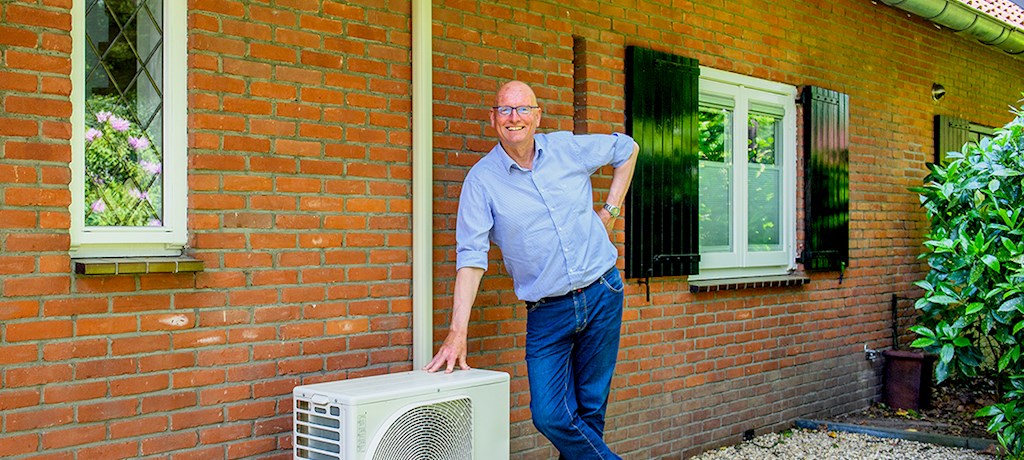 Warmtepomp eigenaar Jan Hoorn staat glimlachend naast de buitenunit van zijn hybride warmtepomp.