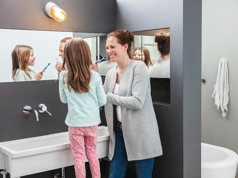 Een glimlachende moeder helpt haar jonge dochter bij het poetsen van haar tanden.