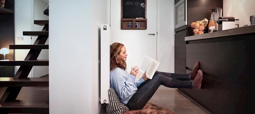 Vrouw zit op de vloer tegen verwarming aan en leest een boek