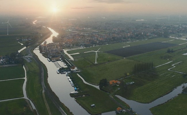 Luchtfoto van windmolens bij dorp met ondergaande zon