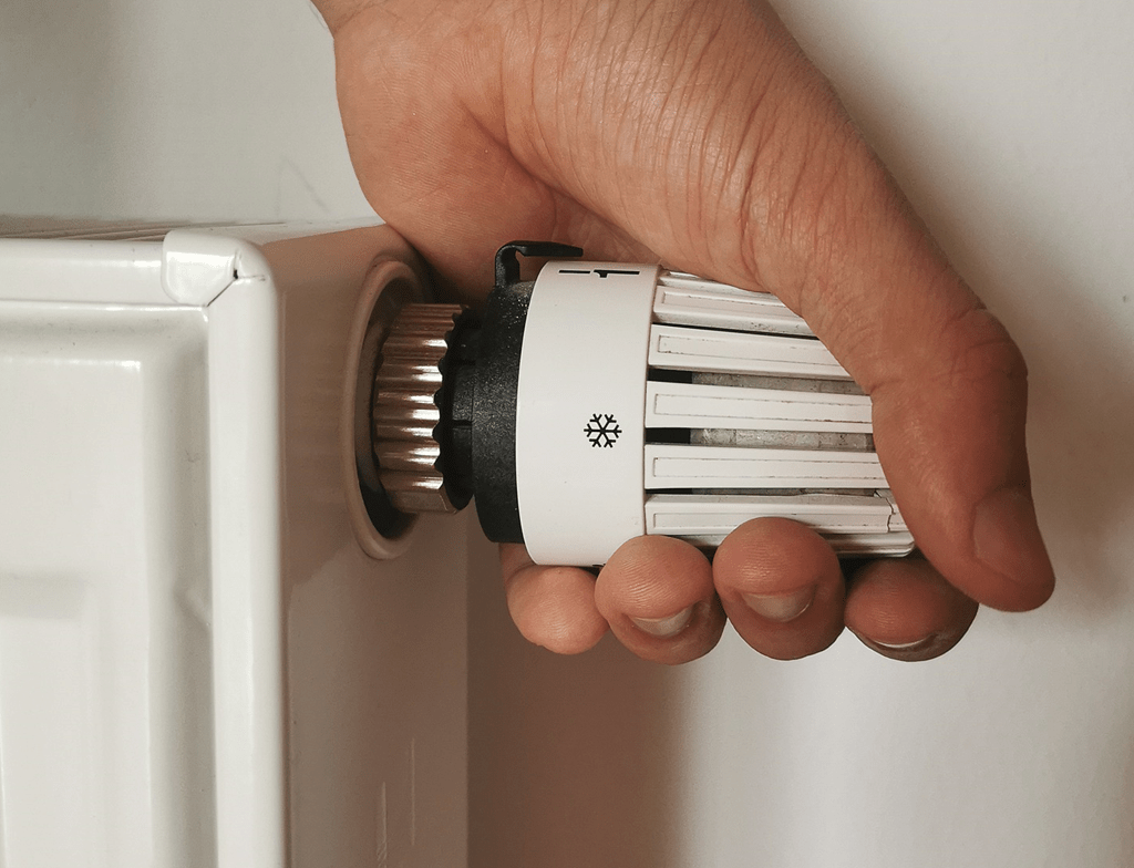 Een hand draait aan de radiatorknop